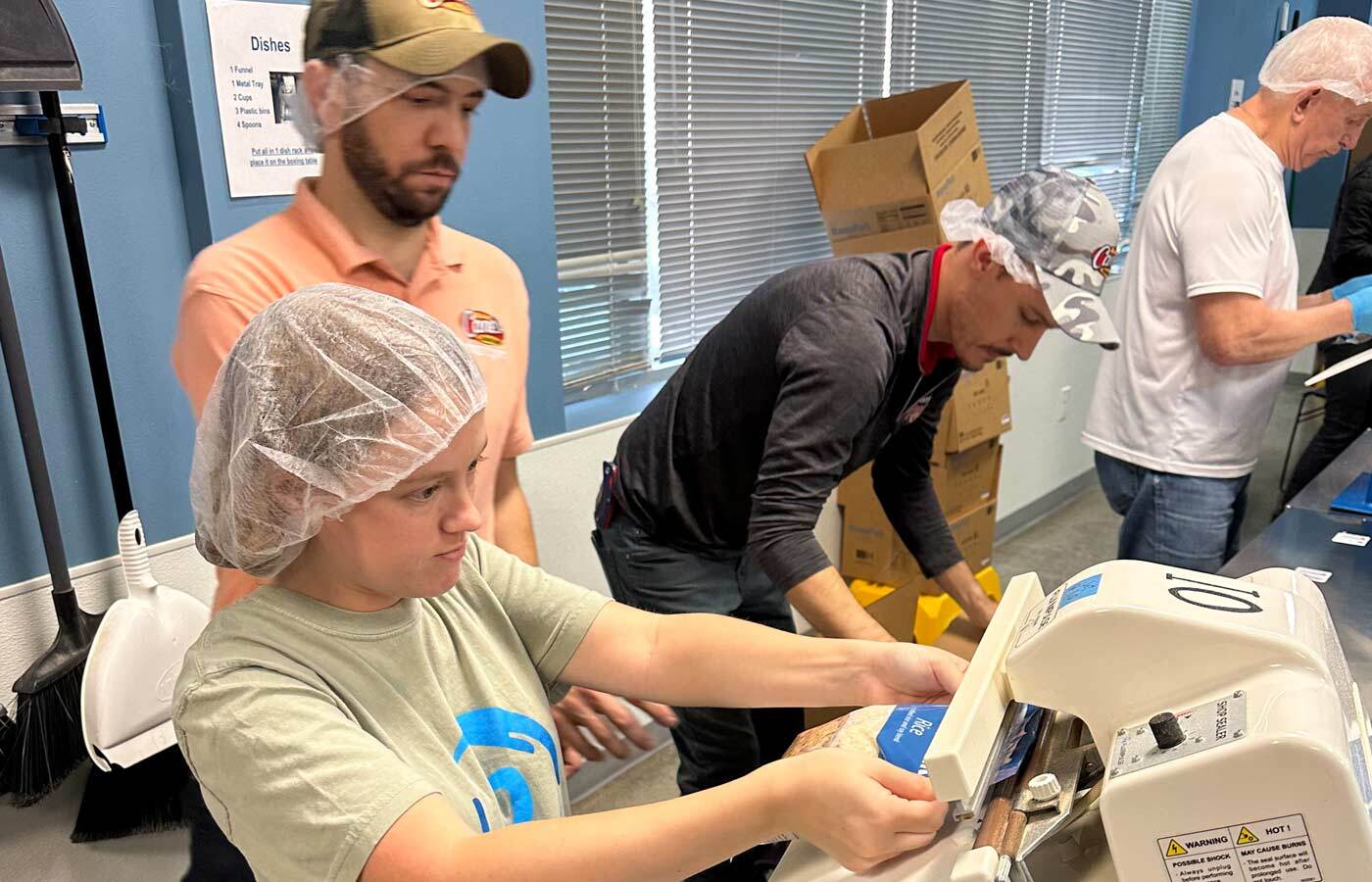 Picture of various people in hairnets packing food.